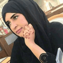 a woman wearing a black hijab with a tattoo on her hand is sitting at a table .