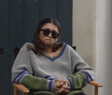 a woman is sitting in a chair wearing sunglasses and a sweater .