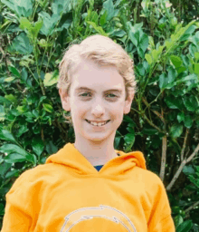 a young boy wearing an orange hoodie smiles for the camera