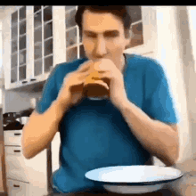 a man in a blue shirt is eating a hamburger while sitting at a table with a bowl of food .