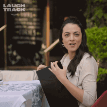 a woman sitting at a table with a menu in front of a sign that says " laugh track "