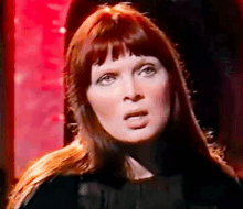 a woman with long red hair and bangs is making a funny face in a dark room .