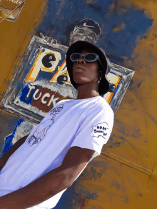 a man wearing sunglasses and a hat stands in front of a sign that says tuck on it