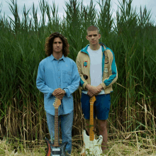 two men standing in a field with their guitars and one has a patch on his jacket that says ' a ' on it