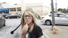 a woman wearing glasses and a hat stands in a parking lot in front of a store that has the word less on the front