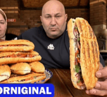 a man holding a sandwich in front of a stack of sandwiches