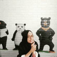 a woman in a black hijab stands in front of a mural of pandas and bears