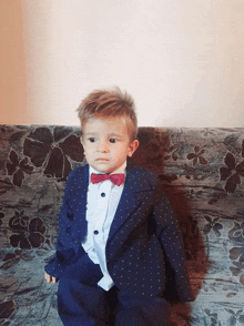 a baby in a suit and bow tie sits on a couch