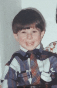 a young boy wearing a plaid shirt and tie is smiling