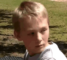 a young boy with blonde hair is sitting at a table looking at the camera .