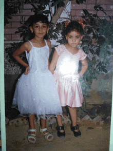 two little girls are posing for a picture and one is wearing a pink dress