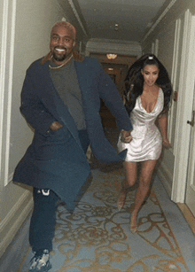 a man in a blue coat and a woman in a white dress are walking down a hallway