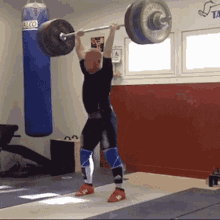 a man is lifting a barbell over his head in a gym with a tae kwon do sign on the wall