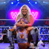 two women wrestling in front of a neon sign that says wow on it