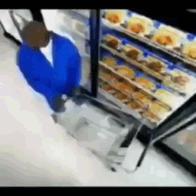 a man in a blue shirt is standing in front of a refrigerator filled with food in a store .