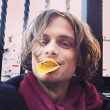 a man wearing a purple scarf has a slice of potato chip in his mouth