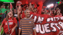 a man in a striped shirt stands in front of a crowd holding a banner that says " guess "