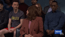 a man in a skull shirt sits in a crowd of people