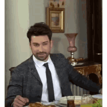 a man in a suit and tie is sitting at a table with a plate of food and a glass of tea .