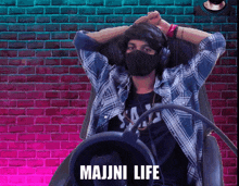 a man wearing headphones and a mask is sitting in front of a brick wall with the words majni life written on it