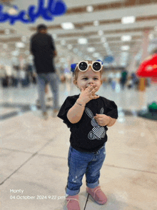 a little girl wearing sunglasses and a black shirt is standing on a tile floor