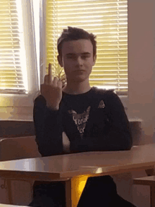 a boy sitting at a desk giving the middle finger wearing a shirt that says foxie