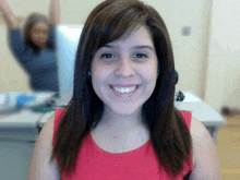 a woman in a red tank top smiles in front of a computer