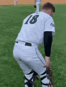 a baseball player wearing a white uniform with the number 18 on the back is kneeling on the field .