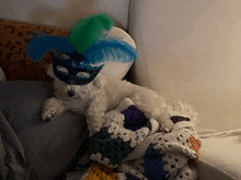 a small white dog wearing a mask and feathers laying on a couch