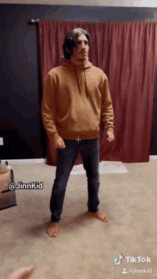 a man in a brown hoodie is standing in front of a red curtain with a tiktok watermark