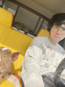 a man wearing glasses sits in the back seat of a car next to a dog