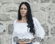 a woman in a white crop top is standing in front of a stone wall with the words buona notte below her