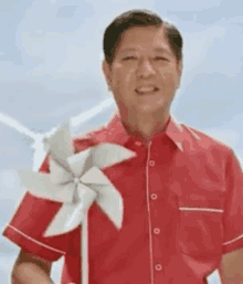 a man in a red shirt is holding a pinwheel in front of wind turbines .