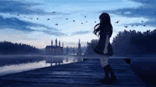 a girl is standing on a dock overlooking a lake with birds flying in the sky .