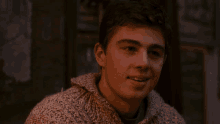 a young man in a sweater is smiling and looking at the camera