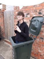 a young man standing next to a trash can that has the lid open