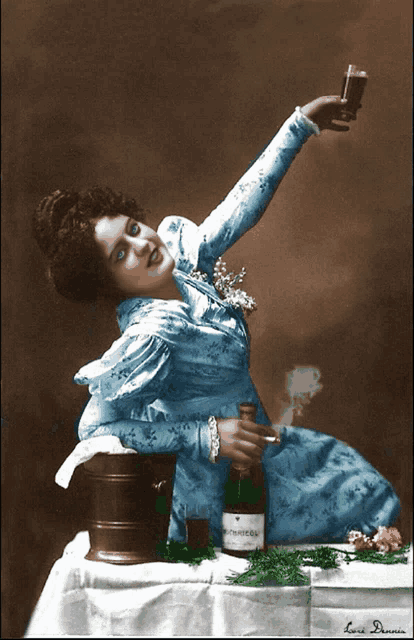 a woman in a blue dress is sitting at a table holding a bottle of prosecco