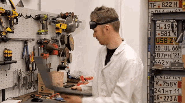 a man in a lab coat is working on a piece of metal in front of a wall of license plates