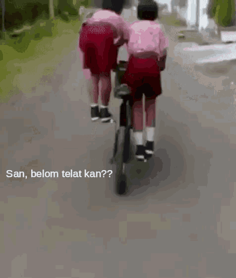 two children are riding a bicycle on a road with the words san , belom telat kan written on the bottom .