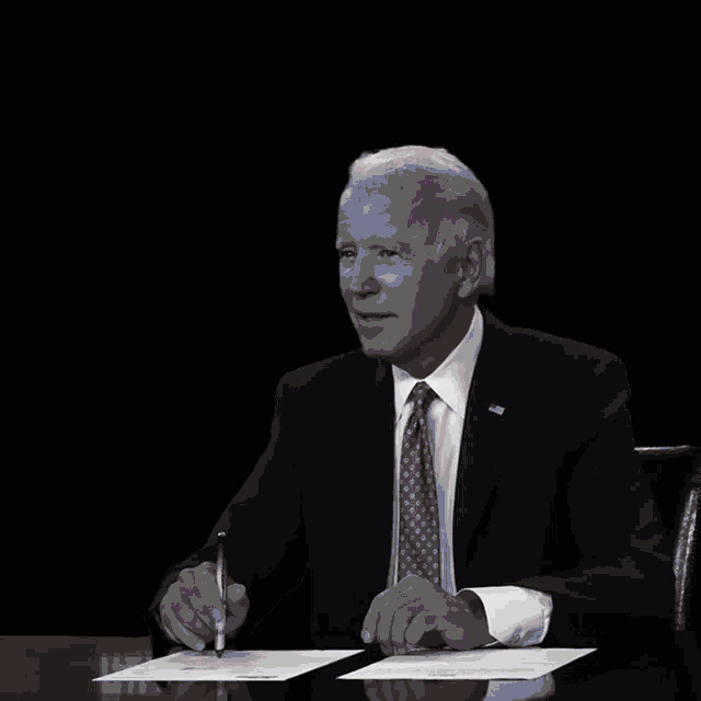 a man in a suit and tie is sitting at a desk with a sign that says student loans paused