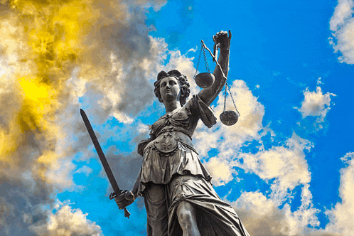 a statue of justice holding scales and a sword against a cloudy sky