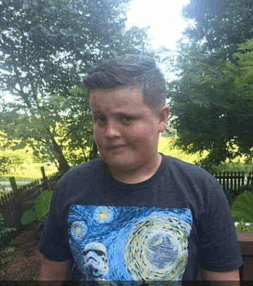 a young boy wearing a star wars t-shirt stands in front of a fence