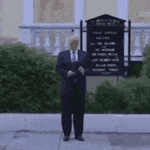 a man in a suit and tie is standing on a sidewalk in front of a sign that says " all are welcome "