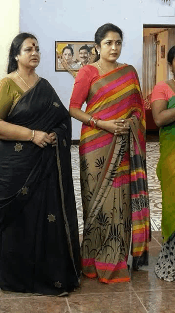 a woman in a black saree stands next to another woman in a striped saree