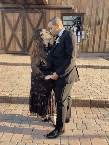 a man and a woman kissing in front of a wooden barn