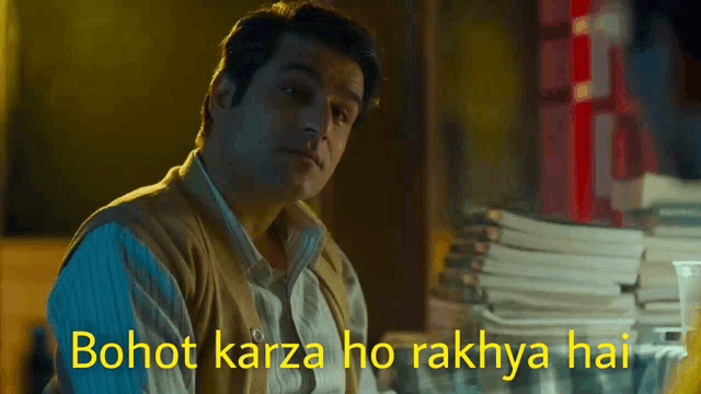 a man sitting in front of a stack of books with the words bohot karza ho rakhya hai written in yellow