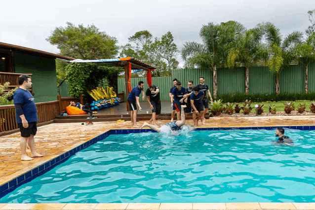 a group of people are jumping into a swimming pool and one of them is wearing a blue shirt that says ' a '