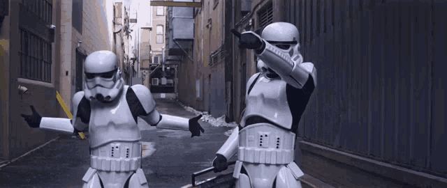 two stormtroopers are standing in an alleyway with their arms outstretched and one is doing a dab