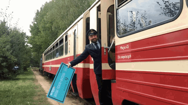 a man holding a blue sign that says ' polska ' on it in front of a red and white train