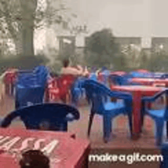 a group of people are sitting at tables and chairs in a restaurant in the rain .